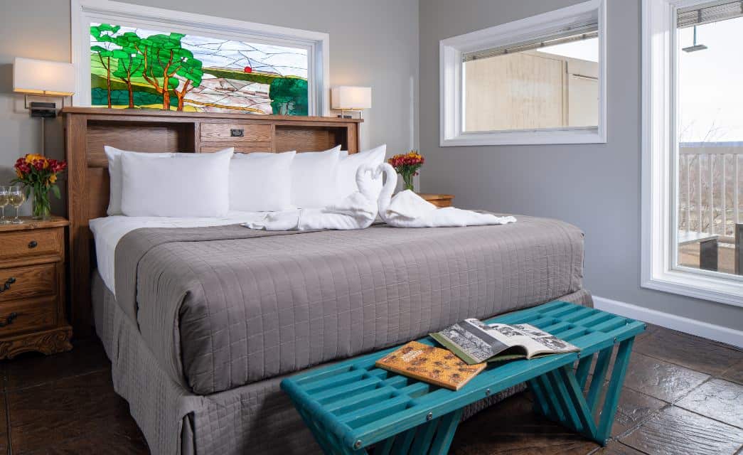 Large bedroom suite with light gray walls, tiled flooring, wooden headboard, white bedding, gray comforter, and turquoise wooden bench