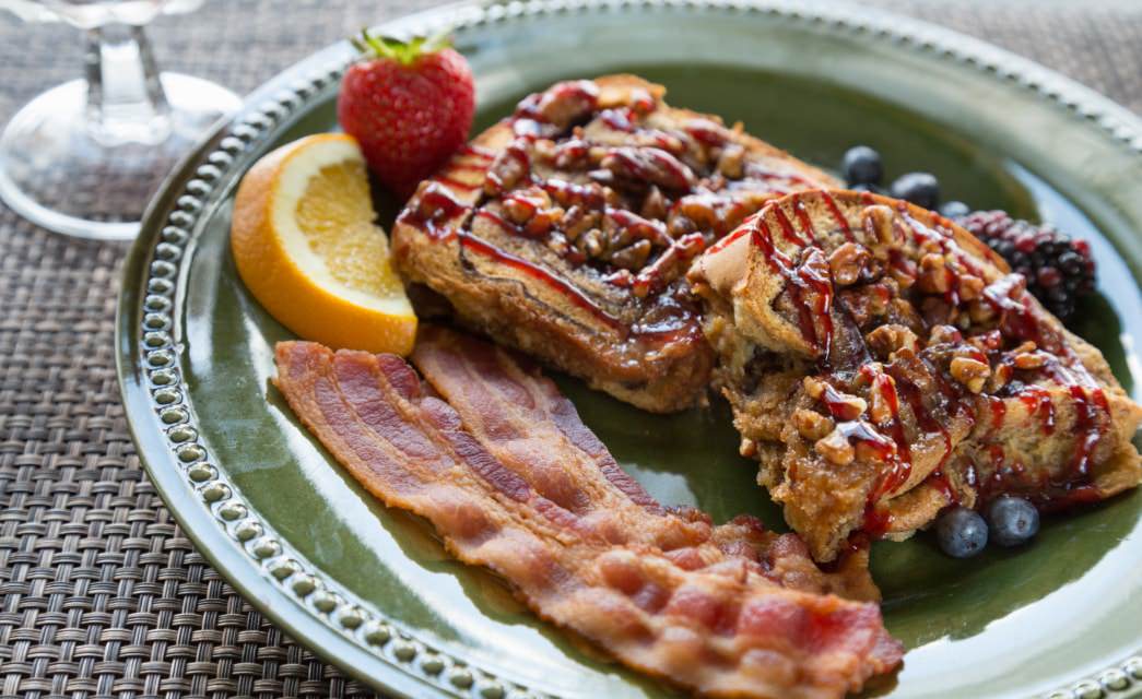 Close up view of stuffed french toast, bacon, and fruit on green plate