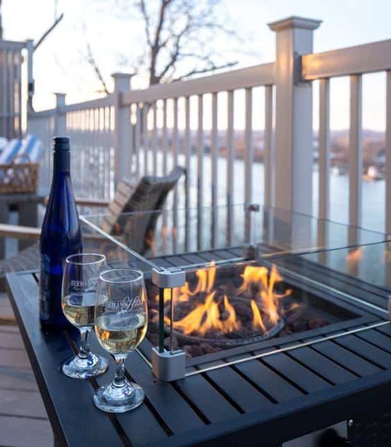 Close up view of lighted table fire pit with glasses of white wine and view of river in the background