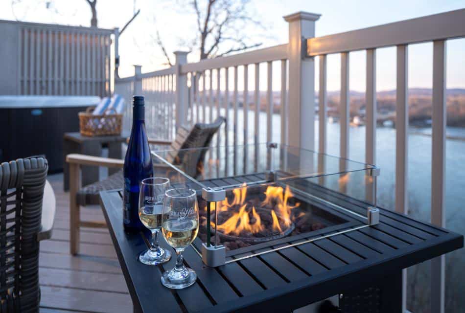 Close up view of lighted table fire pit with glasses of white wine and view of river in the background