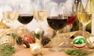 Several wine glasses filled with red and white wine surrounded by colorful, sparkling christmas bulbs