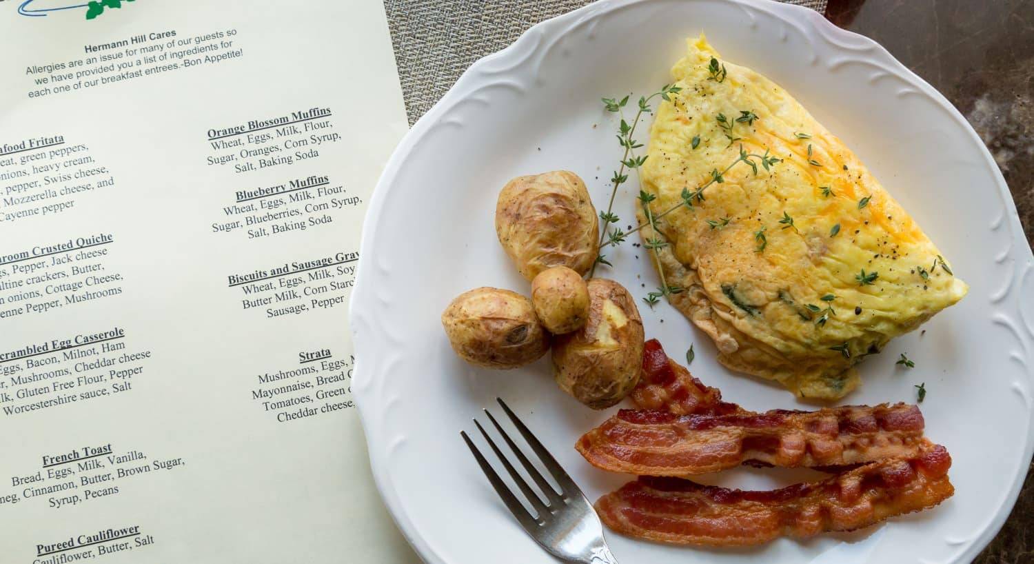 Close up view of breakfast menu and white plate with omelette, bacon, and potatoes